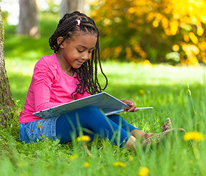 Mädchen sitzt unter Baum und schaut in ein Buch